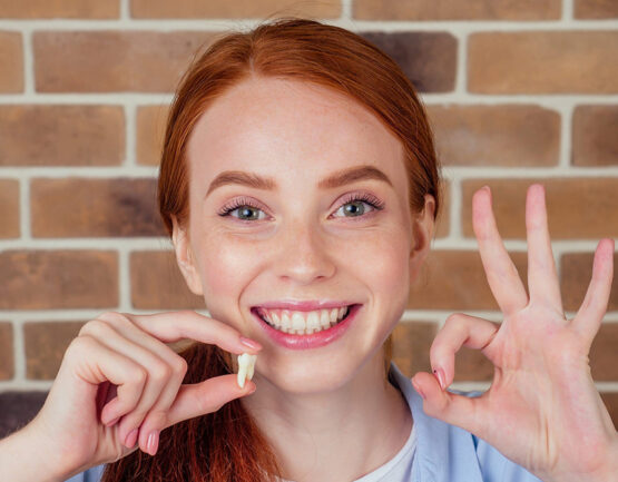 Girl is smiling while she hold a white tooth